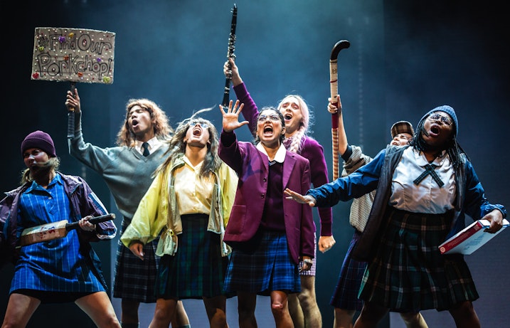 A school girl group in uniform singing and dancing on a stage